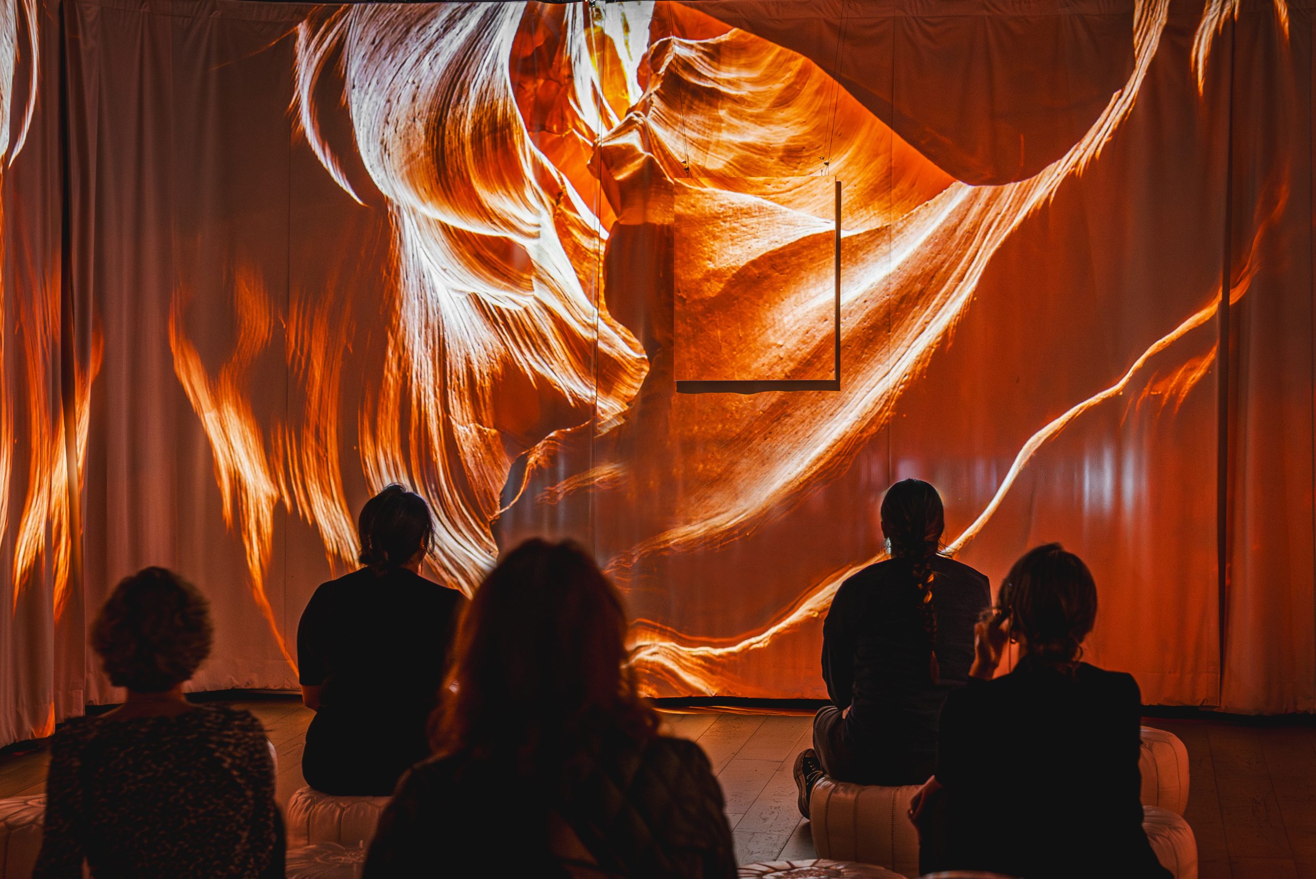 Seated guests watch a glowing orange slot-canyon image projected across the walls at Davy Fiveash's art show