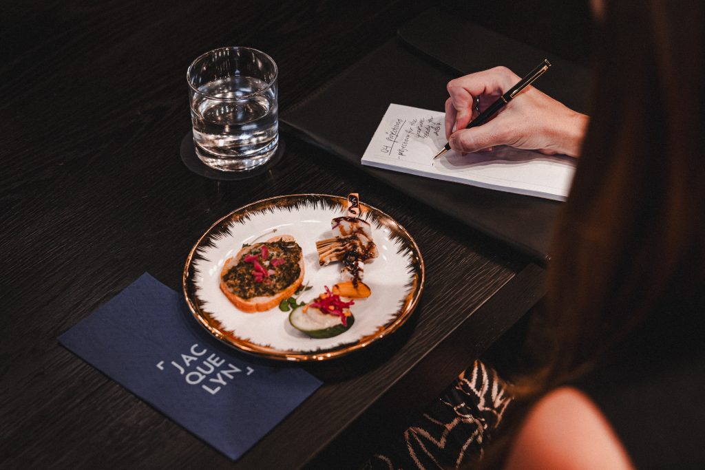 Small plate of bites beside a water glass as a guest takes handwritten notes at a Boardroom meeting