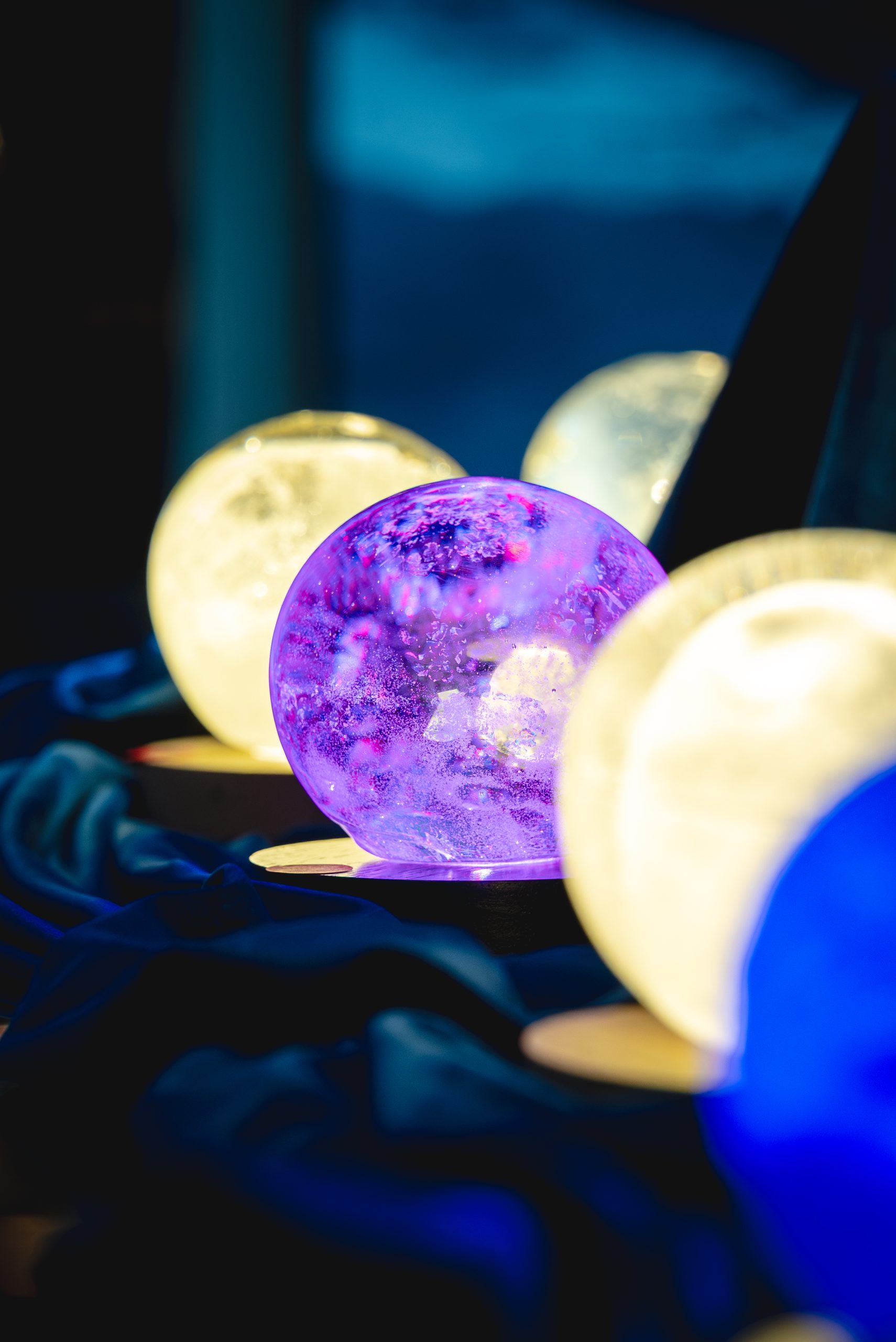 Glowing glass moon orbs in white, purple and blue, part of Anne E. Del Core's moon-inspired exhibition